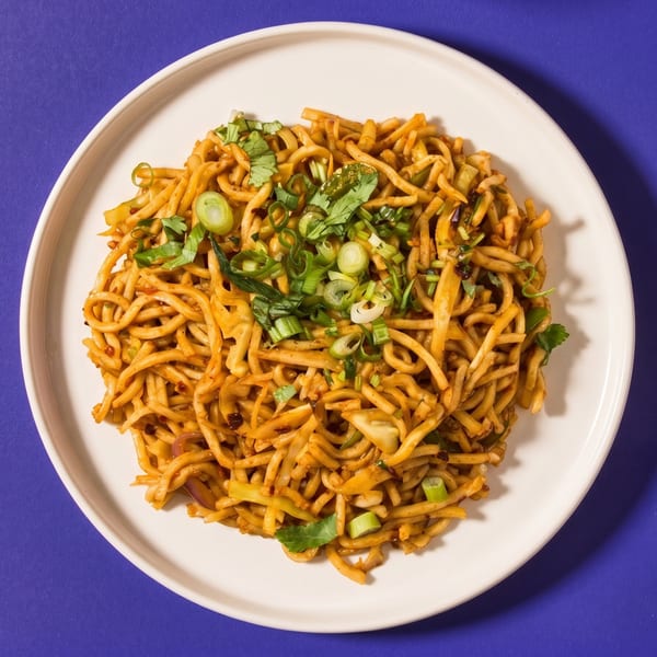 Close-up of stir-fried noodles with green onions and cilantro on a white plate.