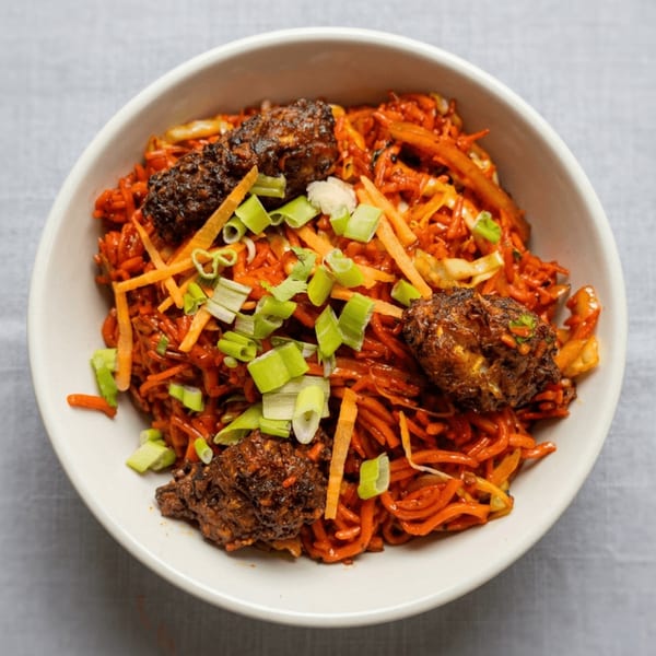 A white bowl filled with orange noodles, topped with dark brown meat and green onions.