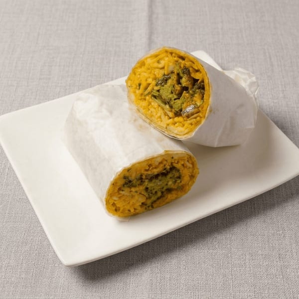 Two halves of a burrito, filled with yellow rice and green vegetables, wrapped in white paper on a plate.