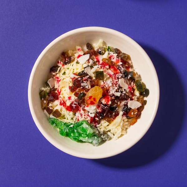 Overhead view of a white bowl filled with a dessert topped with colorful dried fruits and coconut flakes.