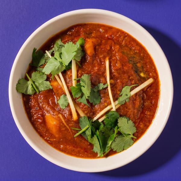 A white bowl of rich red curry, garnished with fresh green cilantro and thin ginger strips.