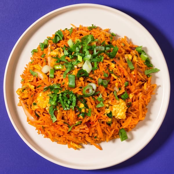 A white plate filled with orange fried rice, topped with green onions and cilantro.