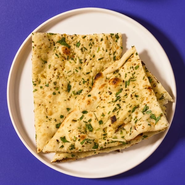 Golden naan bread, sprinkled with green herbs and sesame seeds, on a white plate.