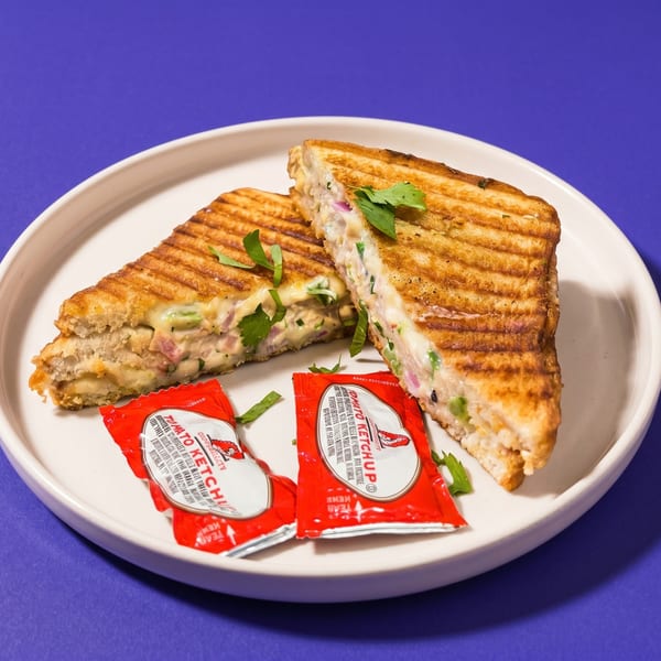 Two halves of a grilled sandwich with creamy filling and cilantro, served with ketchup packets.